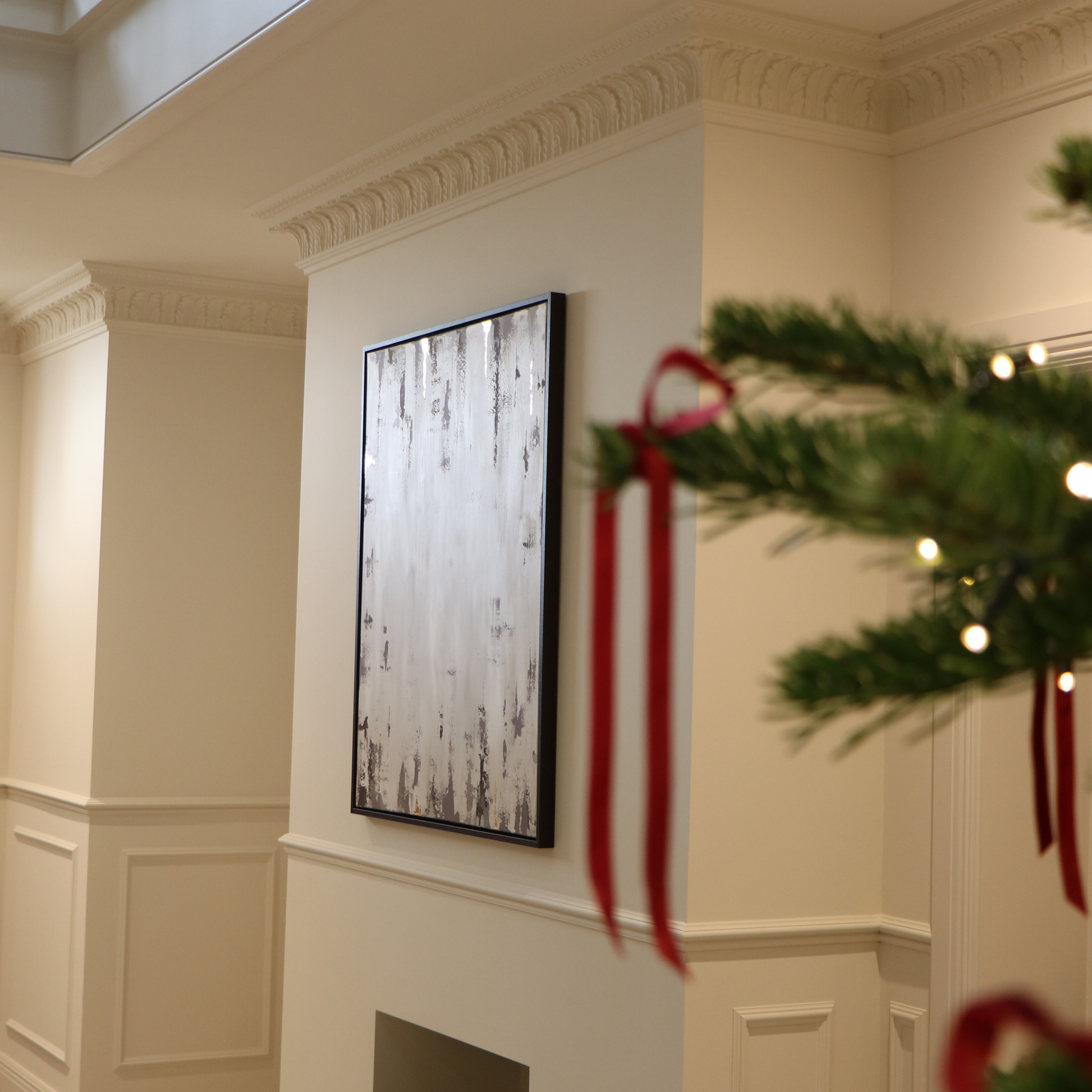 Decorative wall art on a cream wall with a Christmas tree branch in the foreground.