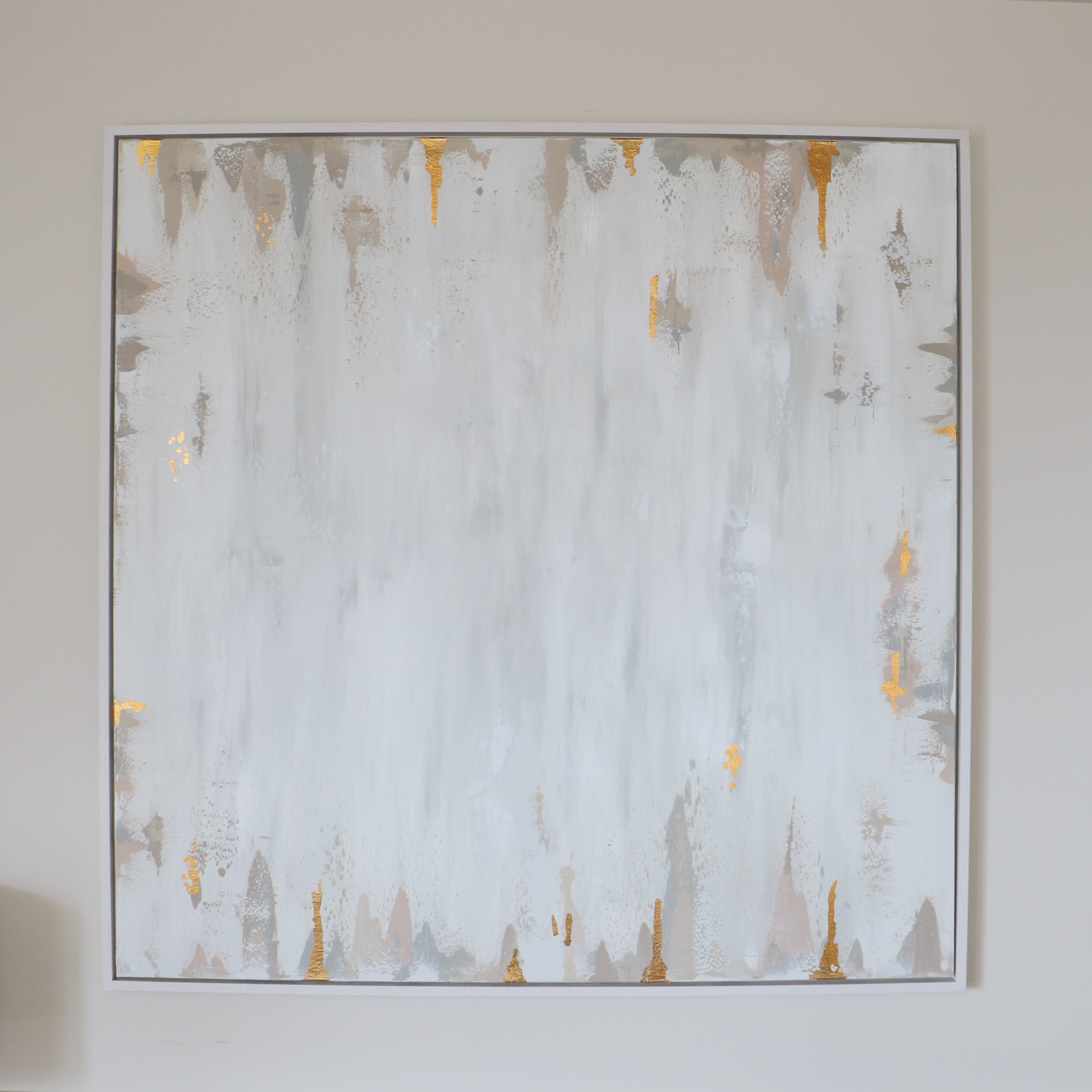 Abstract painting with splashes of gold and beige on a cream wall